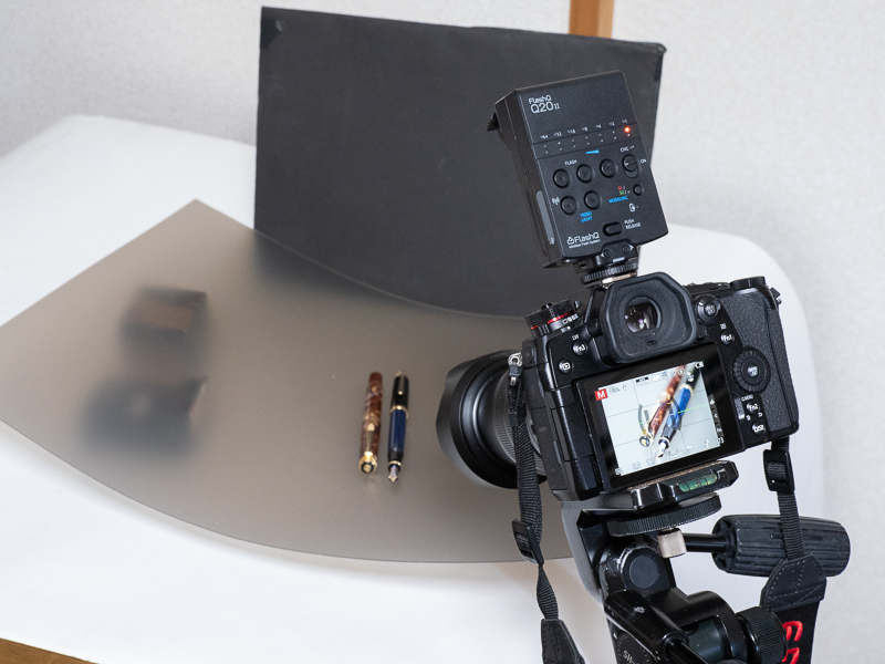 万年筆の撮影の様子。プラ板を浮かせて、下にQ20IIを設置した。また万年筆の後方に余計な光が反射しないよう、黒レフを置いている。