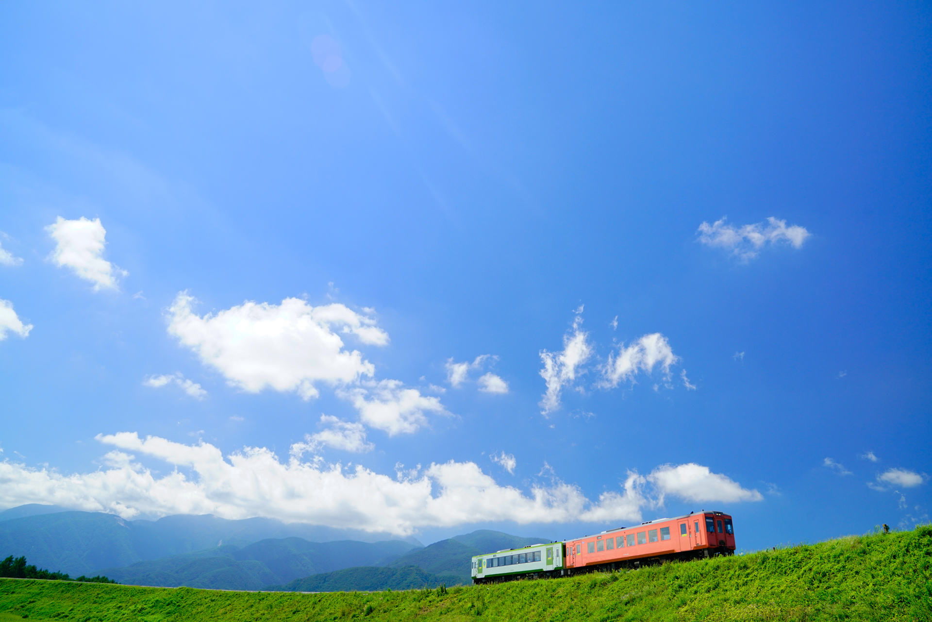 「小淵沢の大カーブ」の内側から24mmで撮影。青空を大きく入れて、少し画面を傾けることでカーブをダイナミックに表現しています。奥に見えるのは南アルプスの山々。カーブの内側からの撮影は、北から南にカメラを向けるので終日逆光気味の光線になります。ただ、作例のように日の長い季節の午前中からお昼前後にかけて、カーブの奥のほうを選べば、列車のサイドにも光を回すことができます。<br>ソニーα7R II　FE 24-70mm F2.8 GM（24mm）　絞り優先オート（F6.3、1/400秒）　ISO 400　WB:太陽光