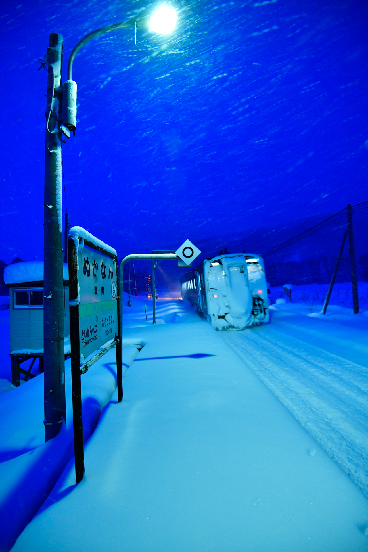 まずご紹介するのは、北海道の原野のなかにポツンとホームがある情景から、ファンも多い宗谷本線の糠南駅。始発の下り列車で下車したら、除雪される前でした。まだ足跡がない雪のホームは雰囲気最高です。周囲には数件の家があるだけですが、ちゃんと7時頃までには地元の人によってきちんと除雪されるから驚きです。こんなにちいさな駅でも、やはりこの土地の玄関なんだなぁと実感しました。<br>ニコンD850　AF-S NIKKOR 16-35mm f/4G ED VR（16mm）　絞り優先オート（F4.0、1/30秒）　ISO 2000　WB:電球　風景　<a href="https://goo.gl/maps/k2H2j3NDyh7Rxoox8" class="n" target="_blank">[GoogleMaps]</a>