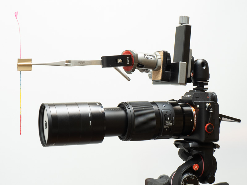 この作例で使ったのはソニーα7R IV＋シグマ 70mm F2.8 DG MACRO。接写リング不要。線香花火を支持するために、ホットシューに雲台や逆作用ピンセットなどを取り付けた。線香花火が燃えて短くなってきたら2WAYフォーカシングレール（Kenko製）を使って位置を調整する。