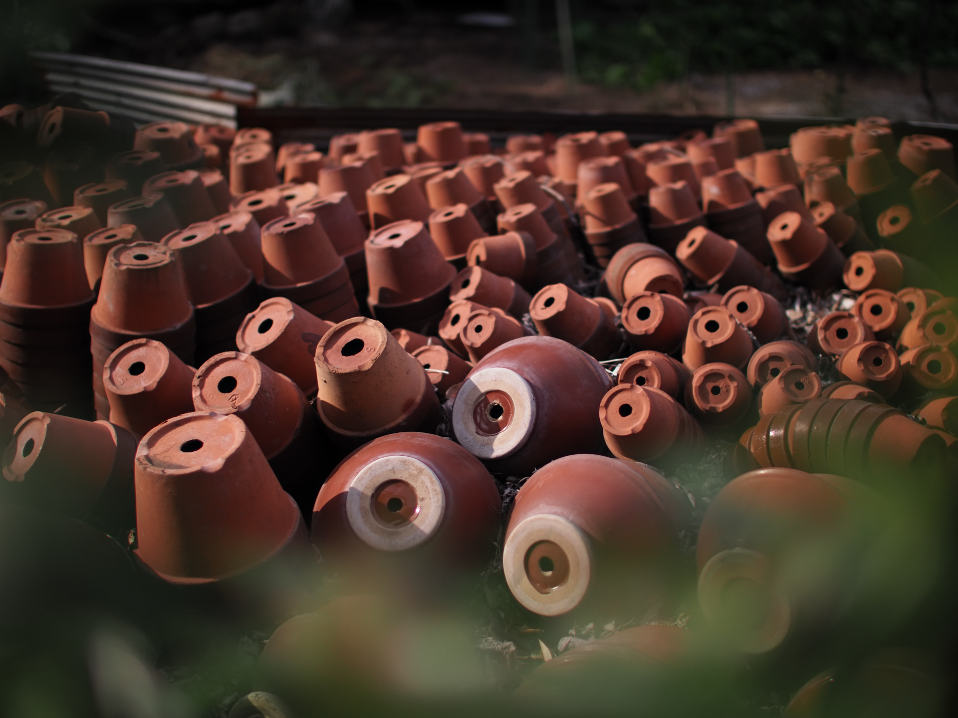 垣根の隙間から花屋さんの裏庭に積まれた植木鉢を撮影してみました。撮影距離は2.5mくらいですが、合焦点の鉢をうまく浮き上がらせてくれました。<br>OM-D E-M1 Mark II　SUPER NOKTON 29mm F0.8 Aspherical（F0.8・1/12,800秒）ISO 200