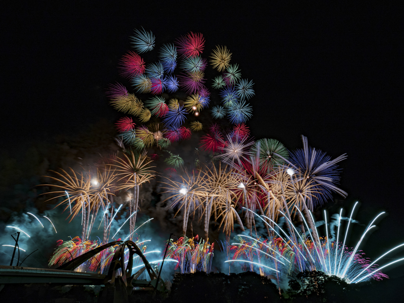 豊田市で開催された豊田おいでんまつり花火大会。色とりどりの花火が夜空を染め上げる見事なワイドスターマインだ。広大な画角を生かして、たくさんの花火を1枚に収めた<br><span class="fnt-85">PEN-F / M.ZUIKO DIGITAL ED 7-14mm F2.8 PRO / 7mmmm（14mm相当） / マニュアル露出（F8、1/2秒×151枚） / ISO 200 / WB:3,300K / ライブコンポジット</span>