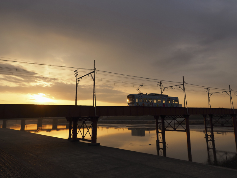 朝日に電車のフロントガラスがきらりと輝く。このタイミングはごく一瞬だ。OM-Dの高速連写と、M.ZUIKO DIGITAL ED 12mm F2.0の逆光耐性を信じてシャッターを切った<br><span class="fnt-85">OLYMPUS OM-D E-M1 Mark III / M.ZUIKO DIGITAL ED 12mm F2.0 / 12mm（24mm相当） / 絞り優先AE（F3.5、1/1,000秒、-0.7EV） / ISO 200 / WB:5,300K</span>