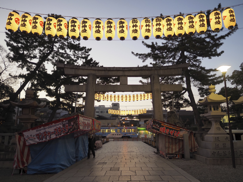 秒単位で暮れていく空、提灯の明かりが浮かび上がる。ISO感度を上げずに後ろを走る電車がぎりぎり止まるシャッター速度を稼げるのも開放F2の魅力<br><span class="fnt-85">OLYMPUS OM-D E-M1 Mark III / M.ZUIKO DIGITAL ED 12mm F2.0 / 12mm（24mm相当） / 絞り優先AE（F2、1/100秒、-0.3EV） / ISO 200 / WB:7,500K</span>