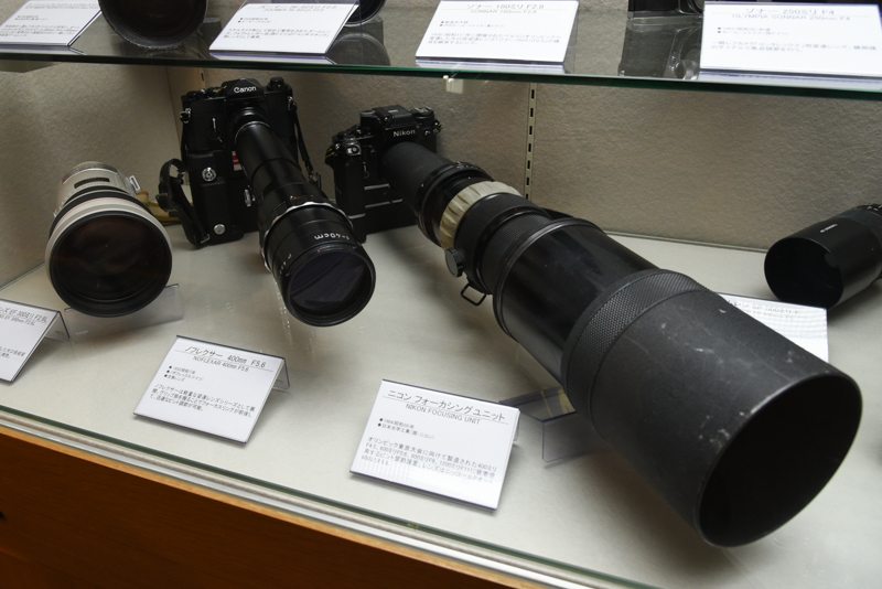 ニコンフォーカシングユニット（右。1964年。日本光学工業：現ニコン）。オリンピック東京大会に向けて製造された400mm F4.5、600mm F5.6、800mm F8、1200mm F11に装着して使用するピント調節装置。写真はニッコールPオート600mm F5.6