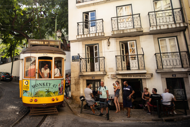 リスボンに暮らす人たちの生活感がムンムンと感じられるカフェと、市民の下駄代わりのトラム。生活とトラムの距離の近さを見せたくて、この場所で撮影しました。よく見ると、物理的にもかなり近いですね（汗）。とっても素直な描写をしてくれるエルマーの味を生かし、奇をてらわない自然な構図で素直に写しました。僕のエルマー50mmはMマウントの第1世代なので、製造は1957年あたり。もう製造から約60年経つレンズですが、必要なところにはシャープ感もあり、もう理論とかを超えた素敵さがあります。<br>ライカM-P（Typ240）　ELMAR 50mm F2.8　絞り優先オート（F3.4、1/1,000秒）　ISO 400　WB:日陰