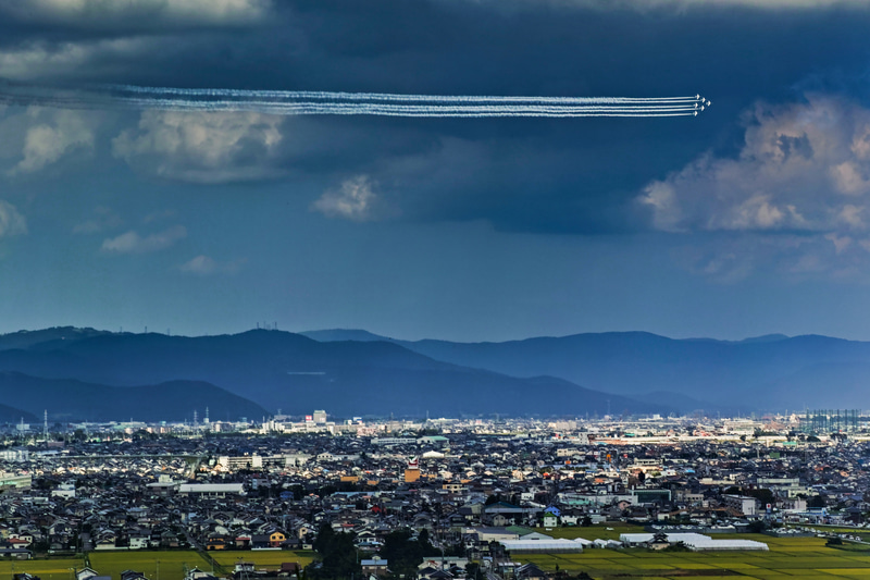 ブルーインパルスの基地がある東松島の夏祭りで、ホームタウン上空を展示飛行する様子。今回のオリンピック/パラリンピック開会式など、祭りや式典などの行事で展示飛行が行われる時は、風景の一部として撮るのも面白いものです。<br>SIGMA dp3 Quattro・Conversion Lens 1.2X FT-1201・1/250秒・F7.1・ISO 100（トリミング）