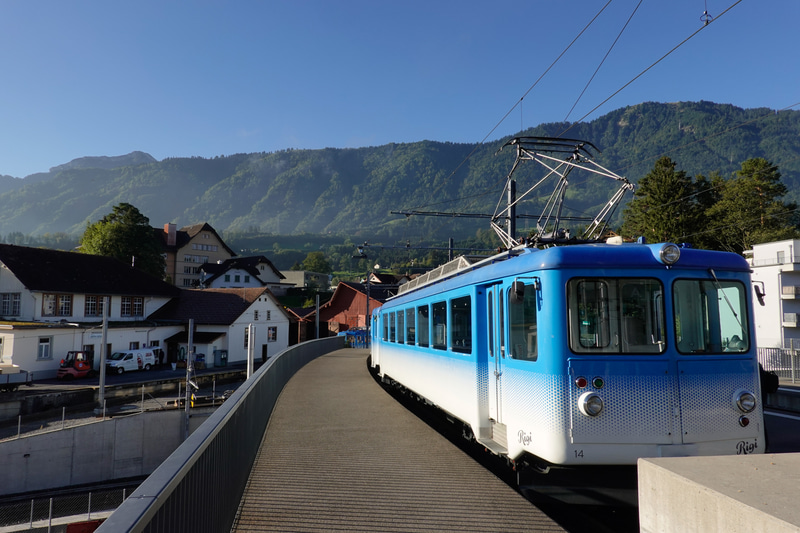 リギ鉄道の起点であるアルト・ゴールダウ駅は、驚くことに国鉄を跨ぐ跨線橋の上にありました。跨線橋を上ると、青白ツートンのかわいい電車がお出迎えです。このリギ鉄道はルツェルン州とシュヴィーツ州にまたがるリギ山へと登る登山鉄道で、リギ山でもっとも標高の高い約1,797mのリギ・クルムまで、鉄道で簡単に登ることができます。<br>ソニーRX100 VI（F9、1/250秒）ISO 125　WB：オート　スタンダード　<a href="https://goo.gl/maps/2qaSCD213LqKTmN26" class="n" target="_blank">[Google Maps]</a>