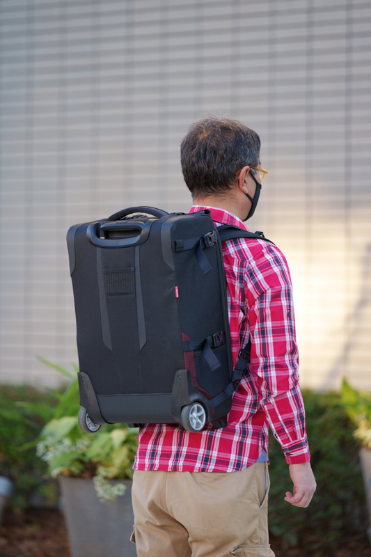 「PL ローラーバッグ SWITCH55」の肩掛けストラップを出して背負ったところ。機内持ち込みサイズとあって、身長171cmの私の場合は腰上で収まる全長だ。