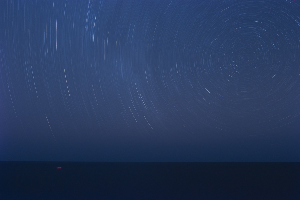 西の海に光跡を引くカシオペア座とペルセウス座。星は1時間で15°動く。この写真では40分露光したので10°だ。40分間の長時間露光で構図をキープし続けるために、頑丈で固定力の強い三脚・雲台が必要だ<br><span class="fnt-85">D500 / AF-S DX NIKKOR 16-80mm f/2.8-4E ED VR / 16mm（24mm相当） / マニュアル露出（F5.6、2,373秒） / ISO 400 / WB:白熱電球</span>