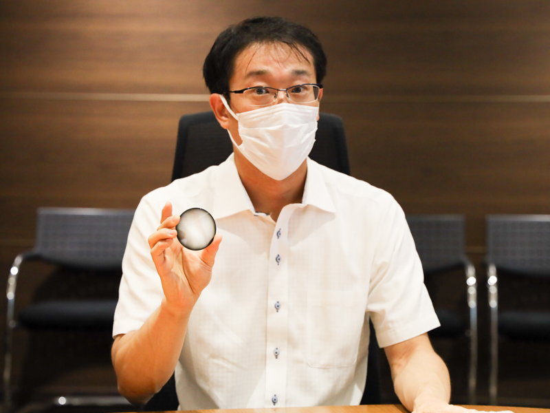 DSコーティングを施したレンズを手にする石橋氏。レンズの周辺部が黒くコーティングされている様子がわかる