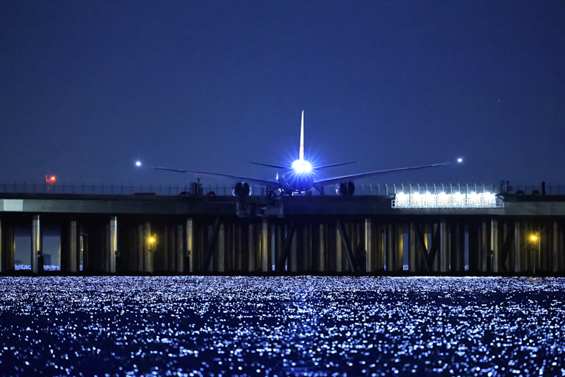 満月が海を照らし普段とは様相が異なる羽田空港D滑走路。望遠レンズとスローシャッターゆえに三脚は必須。ストロボライトがタイミング良く光った瞬間を捉えた<br><span class="fnt-85">EOS R3 / EF500mm F4L IS II USM / 500mm / 絞り優先AE（F4.6、1/30秒、±0EV） / ISO 51200 / WB:3,200K</span>