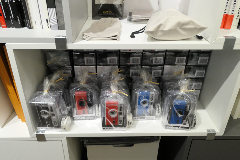 イルフォードのフィルムカメラ（下）と、クリーニングクロス素材の手袋・巾着（上）