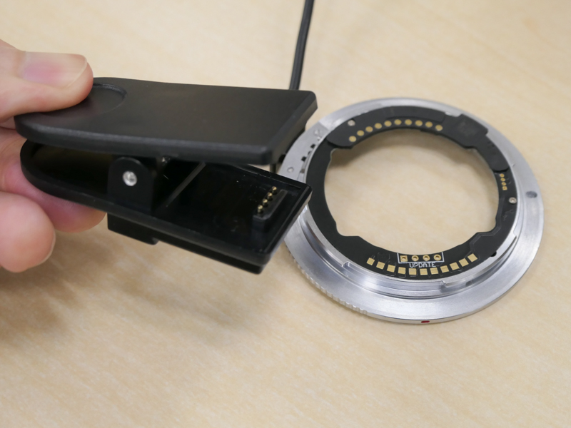 本アダプターは購入後のファームウェアアップデートも可能（試用後6月21日にVer.2.00が公開。今後の更新で動作改善するレンズもあるだろう）。驚くのがその方法で、付属のクリップのような装置でアダプターを挟む。反対側はUSB Type-A端子