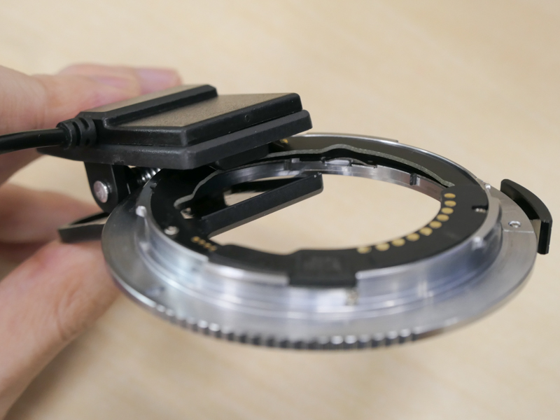 本アダプターは購入後のファームウェアアップデートも可能（試用後6月21日にVer.2.00が公開。今後の更新で動作改善するレンズもあるだろう）。驚くのがその方法で、付属のクリップのような装置でアダプターを挟む。反対側はUSB Type-A端子