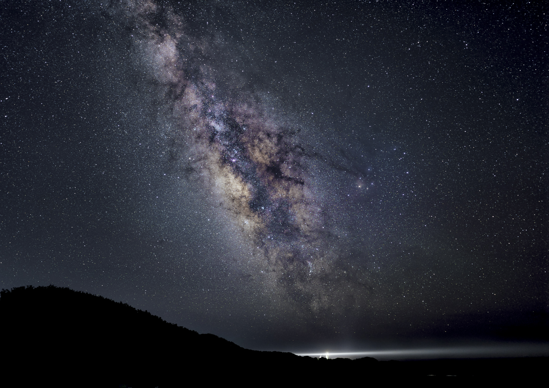 本州最南端にある潮岬灯台を望む駐車場より。ちょうど灯台から天の川の光が噴出しているかのように撮影した。開放F1.4のおかげで、固定１枚撮りでも天の川を申し分なく表現できる<br><span class="fnt-85">α7S III／マニュアル露出（F1.4、15秒）／ISO 3200／WB：オート</span>