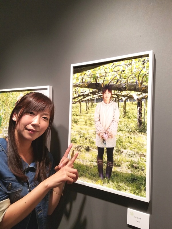 エプサイトの写真展で自分の写真前で写る實川さん