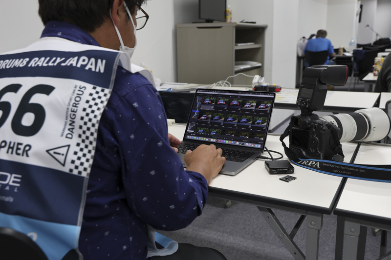 プレスルームで作業する高橋学さん。着ているフォトグラファーズタバードにプログレードデジタルのクレジットが記載されている