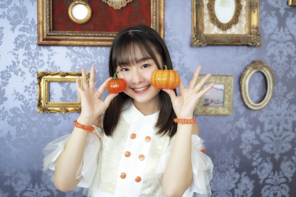 メンバーカラーであるオレンジ色のかぼちゃを持ってスマイル。背景のアンティークなフレームも見せたかったので、絞りは少し絞ってF2.5で撮影しました<br><span class="fnt-85">キヤノン EOS R6 Mark II／RF35mm F1.8 MACRO IS STM／35mm／マニュアル露出（F2.5、1/400秒）／ISO 640／WB：オート</span>