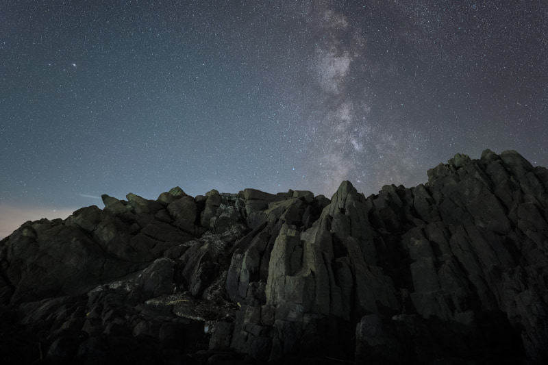 秋田県の海岸沿いで撮影。柱状節理と夏の天の川。撮影時は不安定な岩場に三脚を広げ、低くカメラを設置。石突スパイクの効果もあり、がっちりと固定できた<br><span class="fnt-85">LUMIX S5／SIGMA 20mm F1.4 DG DN</span><br>
