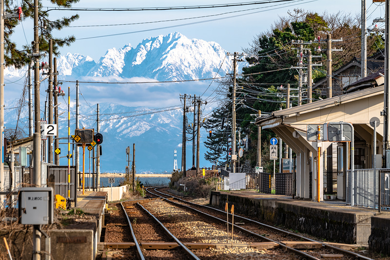 雨晴（あまはらし）駅のホームとその奥には剱岳。JR氷見線の雨晴駅は、富山県高岡市にある海の見える駅。線路が海へ続いているように見えるイメージで構図を作った。<br>ライカSL2／パナソニック LUMIX S 70-300mm F4.5-5.6 MACRO O.I.S.／265mm／マニュアル露出（F11、1/100秒）／ISO 100／WB：オート