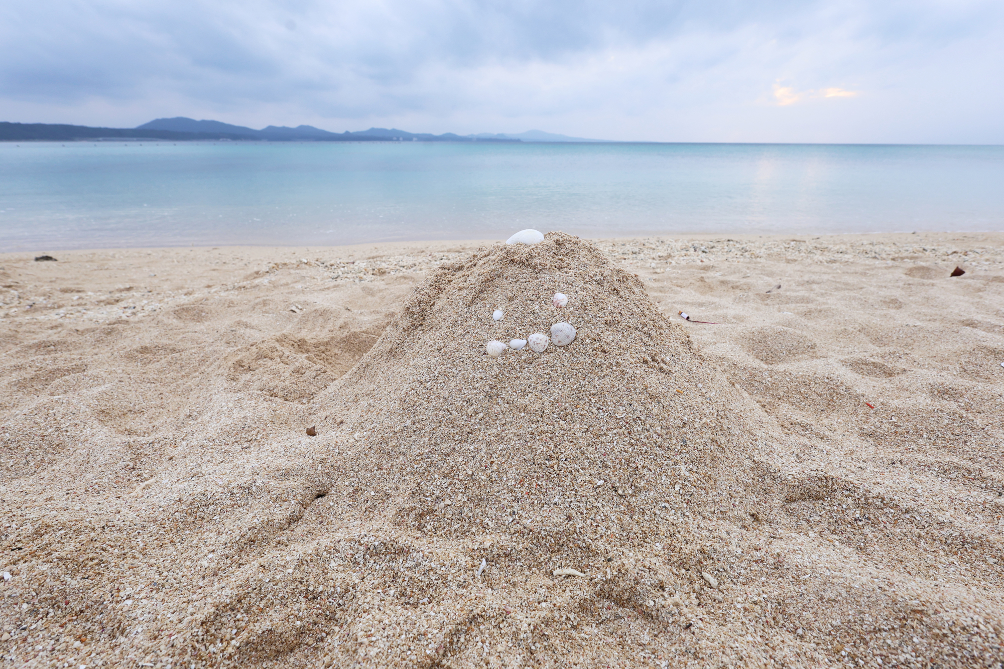 親子が作っていた砂の山に貝殻でできたかわいい顔が。RF15-30mmの広角端で近づき背景の海を入れてローポジションでフレーミング。このような場面ではバリアングルモニターが役に立つ<br><span class="fnt-85">EOS R8／RF15-30mm F4.5-6.3 IS STM／15mm／プログラムAE（F8、1/200秒、+0.7EV）／ISO 400／WB:オート</span>