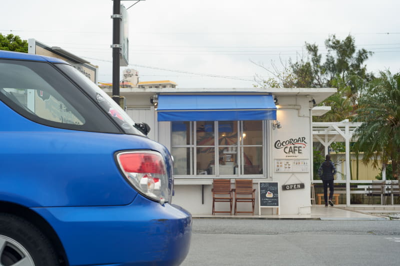 ディテールが残った白い空。ここに青空があれば良かった……と思うけれど、もしも青空だったらこの車と屋根の青に気付かなかったかも。そう思えば空とカフェの白も良し。<br>ライカSL2-S／ノクティルックスM f1.25/75mm ASPH.／絞り優先AE（F8、1/160秒、±0EV）／ISO 200／WB：オート