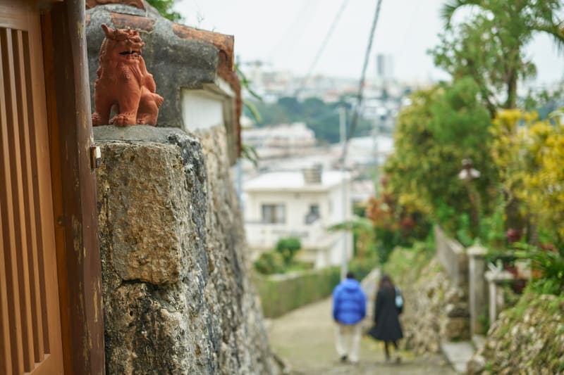 首里の石畳を歩くカップルを見守るシーサー。毎日何人を見守っているのだろう。家によって表情の違うシーサーは、それぞれの個性があって楽しい。<br>ライカSL2-S／アポ・ズミクロンM f2/50mm ASPH.／絞り優先AE（F4、1/800秒、±0EV）／ISO 100／WB：オート