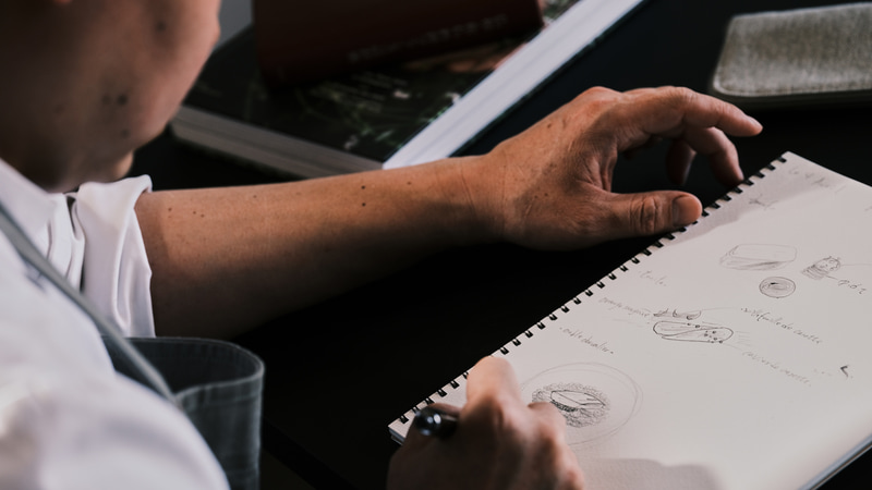 食材をどう魅せるかをイメージするためにスケッチを行うシェフ。その様子をBV-20による微細な角度調整で斜め上から撮影した<br><span class="fnt-85">FUJIFILM GFX100S／GF120mmF4 R LM OIS WR Macro／120mm（95mm相当）／マニュアル露出（F5.6、1/125秒）／ISO 1600／WB：5,300K</span>