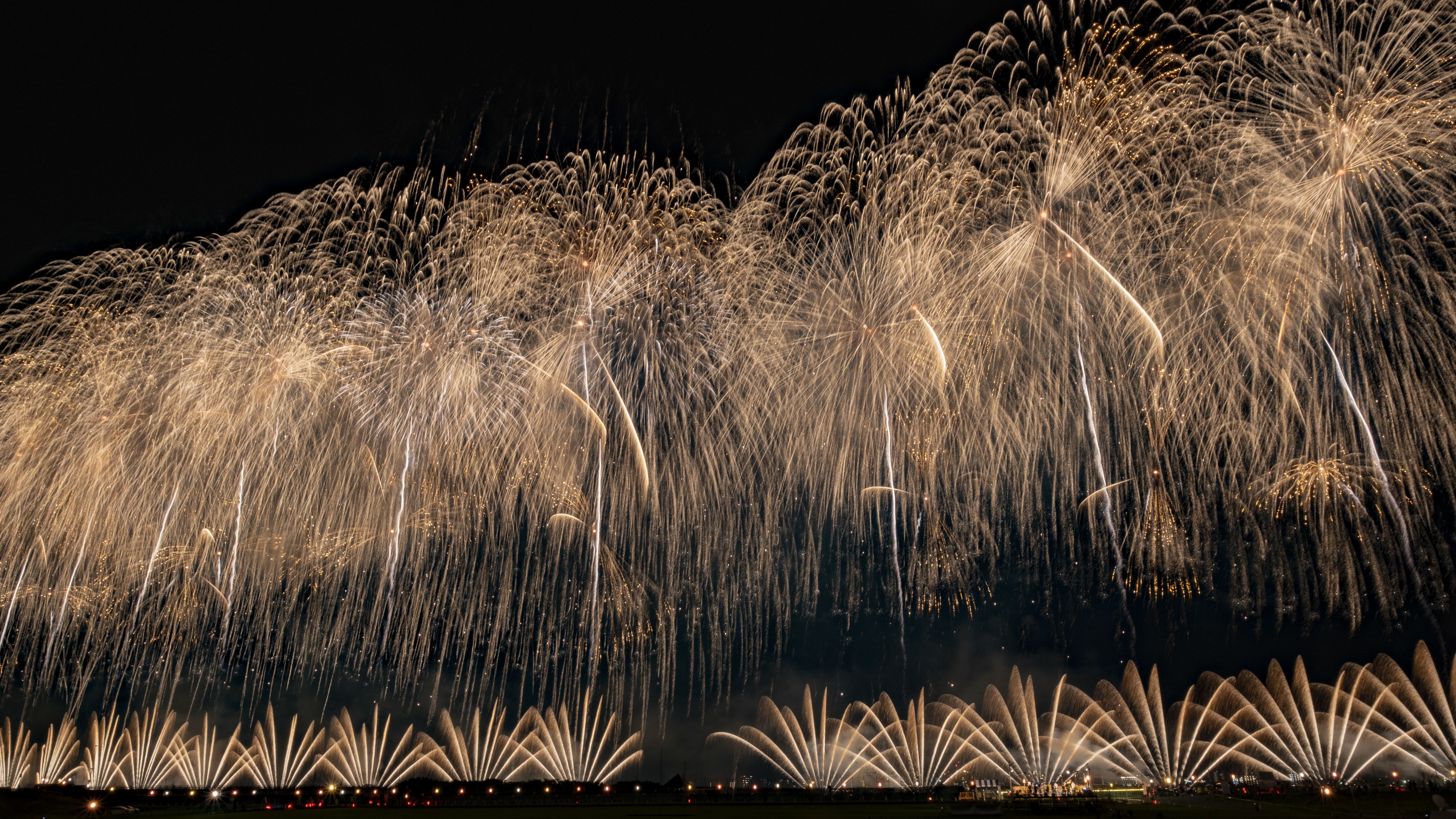 幅2kmのワイドスターマイン「震災復興祈願花火フェニックス」のエンディング。錦冠菊花火の中に鳥型のフェニックスが写っている。ワイド感を出すために16：9にトリミングした（撮影：金武 武）<br><span class="fnt-85">X-T3／XF10-24mmF4 R OIS／13.2mm（20mm）／マニュアル露出（29.0秒、F16）／ISO 160</span>