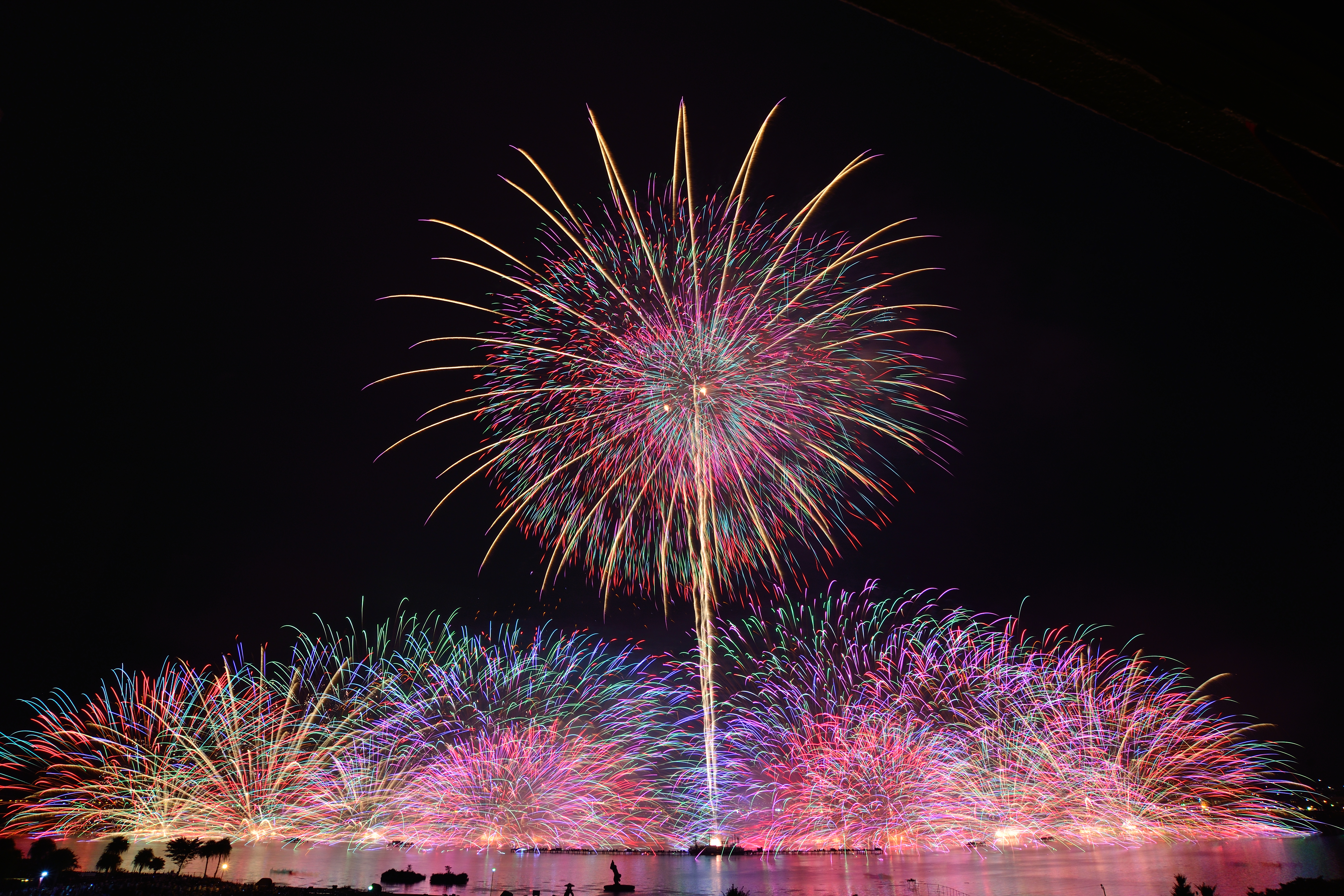 エンディングの水上ワイドスターマイン「Kiss of Fire」。左右から始まり中央に近づいてくる打上演出。花火が沢山重なり過ぎると露出オーバーになるのでレンズの前を隠したり外したりを繰り返して撮影した。（撮影：金武 武）<br><span class="fnt-85">D600／AF-S NIKKOR 18-35mm f/3.5-4.5G ED／18mm／マニュアル露出（3.53分、F11）／ISO 100</span>