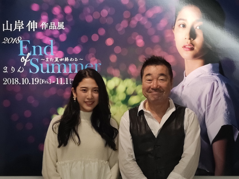 作品展会場内、メインビジュアルのボードの前で茉音ちゃんと