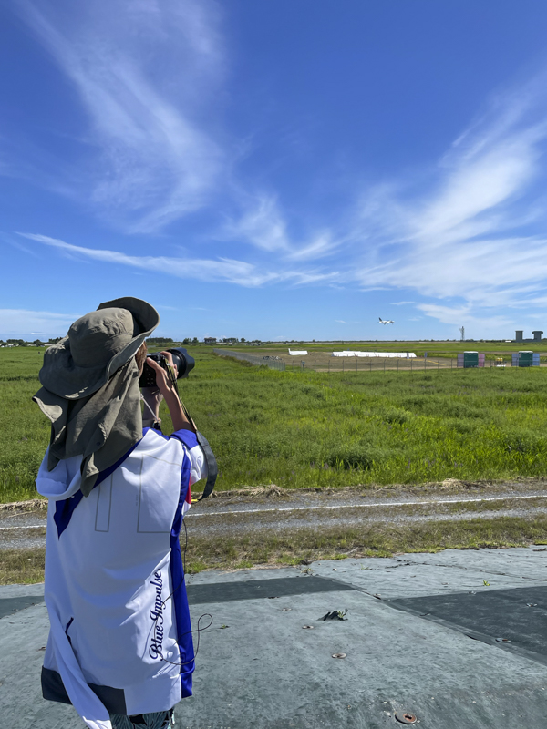 東松島夏まつりの撮影風景。滑走路の向きがわかっていればブルーインパルスの飛行方向もわかるので、混雑を避けた場所で撮影してもOK。基地の近くなら、機体を大きく捉えられます