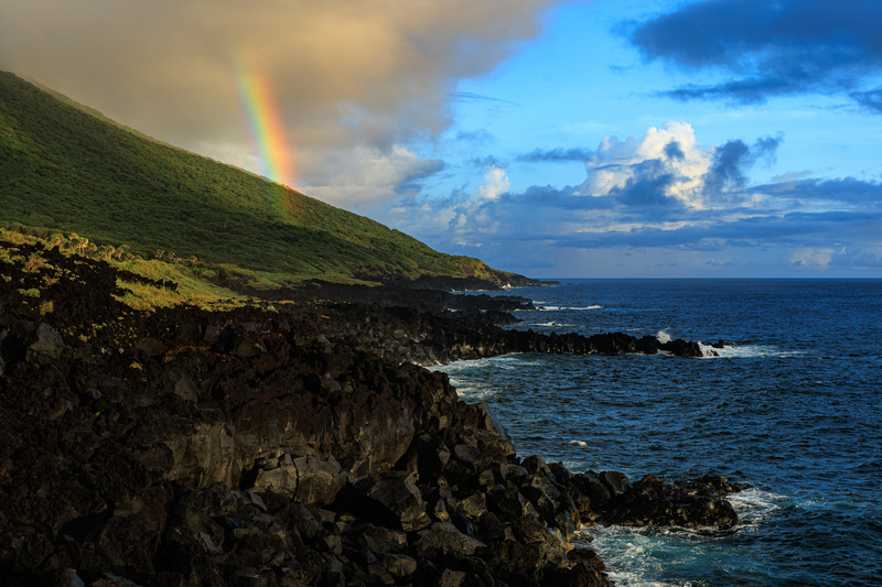 海に流れ込んだ溶岩が作る岸壁に、朝日を浴びた虹がアクセントになった。黒い溶岩の繊細なグラデーションやシャドウのディテールを広いダイナミックレンジが見事に再現してくれる<br><span class="fnt-85">EOS R8／RF24-105mm F4 L IS USM／24mm／絞り優先AE（F8、1/40秒、－1.0EV）／ISO 100／WB：オート</span>