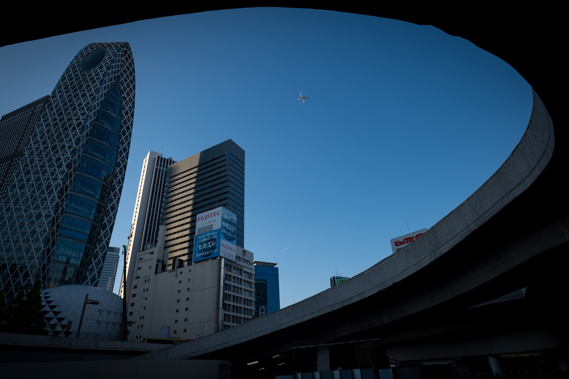 都心上空を飛ぶ飛行機に注目する人はほとんどいなくなりましたが、年寄りには気になる被写体です。再開発中の新宿西口を地下から見てみようという試みであります<br>LUMIX S5IIX／LUMIX S 20-60mm F3.5-5.6／絞り優先AE（20mm・F8・1/1,000秒・-1EV）／ISO 400