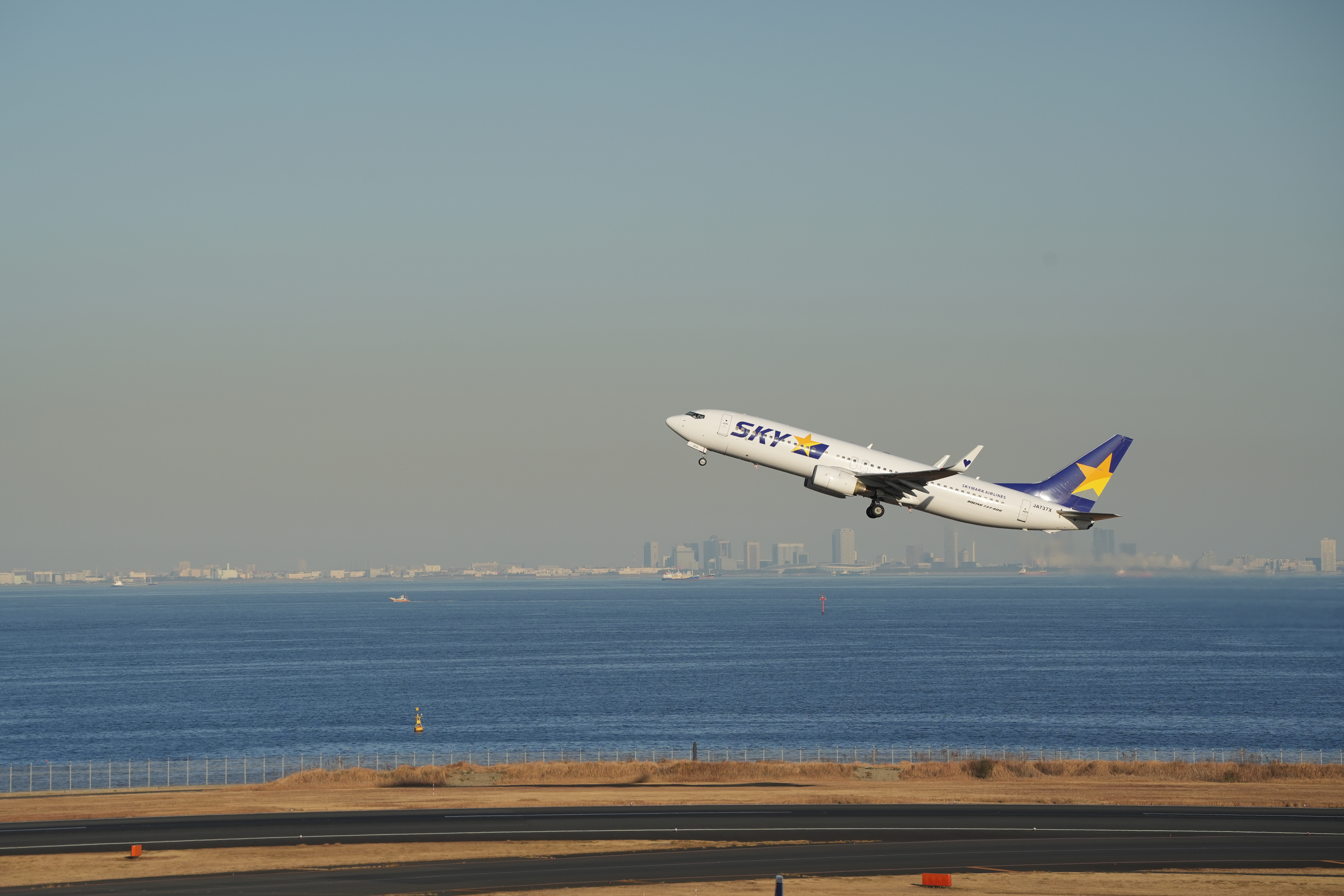 離陸するスカイマーク機。200mmでは焦点距離が足りないかなと思っていたが、200mmで周りの風景を入れた感じも良いなと感じられた1枚だ。<br><span class="fnt-85">α7 IV／SIGMA 70-200mm F2.8 DG DN OS｜Sports／200mm／マニュアル露出（1/2,000秒、F8）／ISO 400／WB: 太陽光</span>