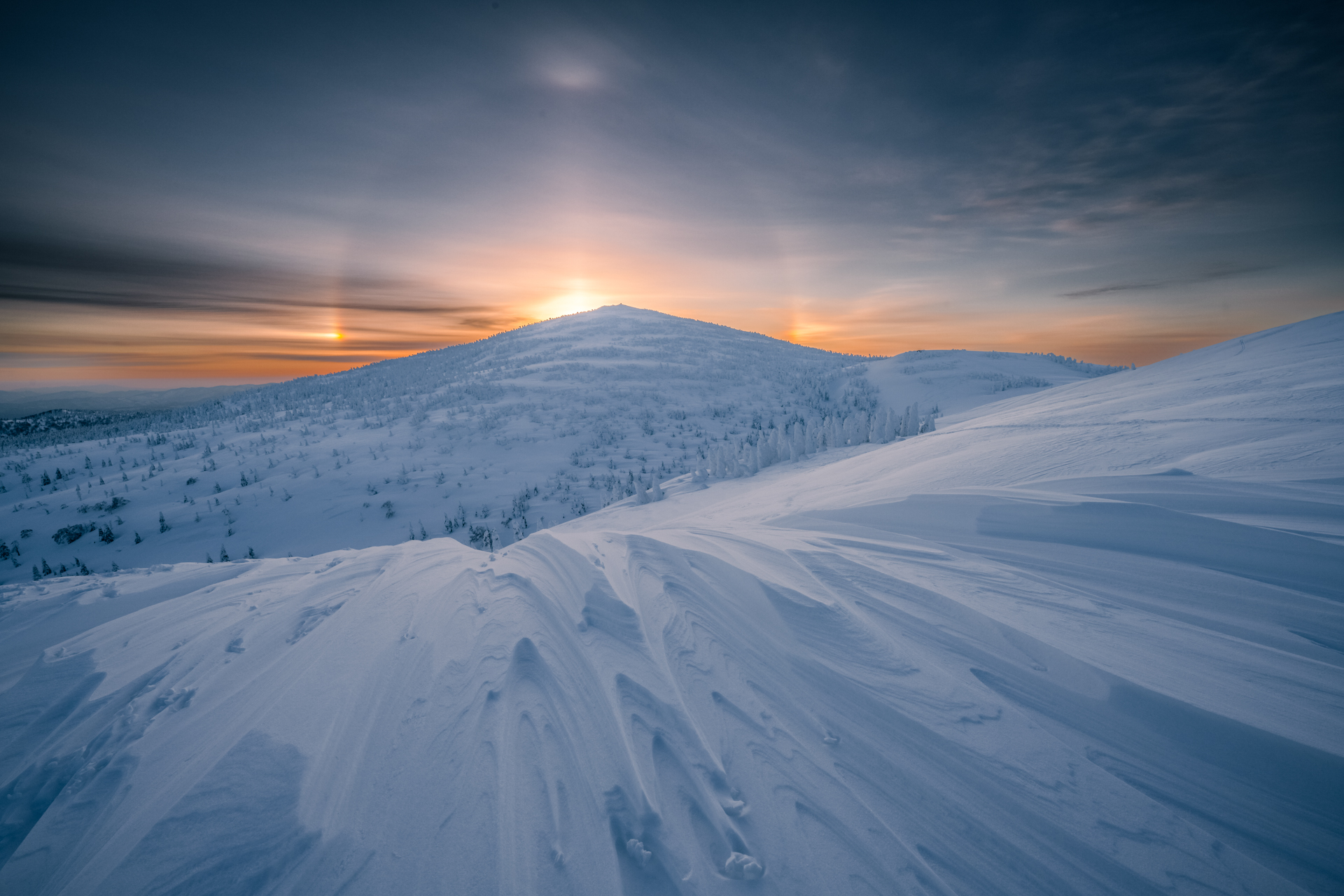 森吉山の山頂にある避難小屋で一晩待機して迎えた朝。雪面すれすれにカメラをセットしてシュカブラ越しに撮ったハロとサンピラーを従えた神々しい朝日<br><span class="fnt-85">Z 7 II／NIKKOR Z 14-24mm f/2.8 S／14mm／マニュアル（1/125秒、F16）／ISO 80</span>