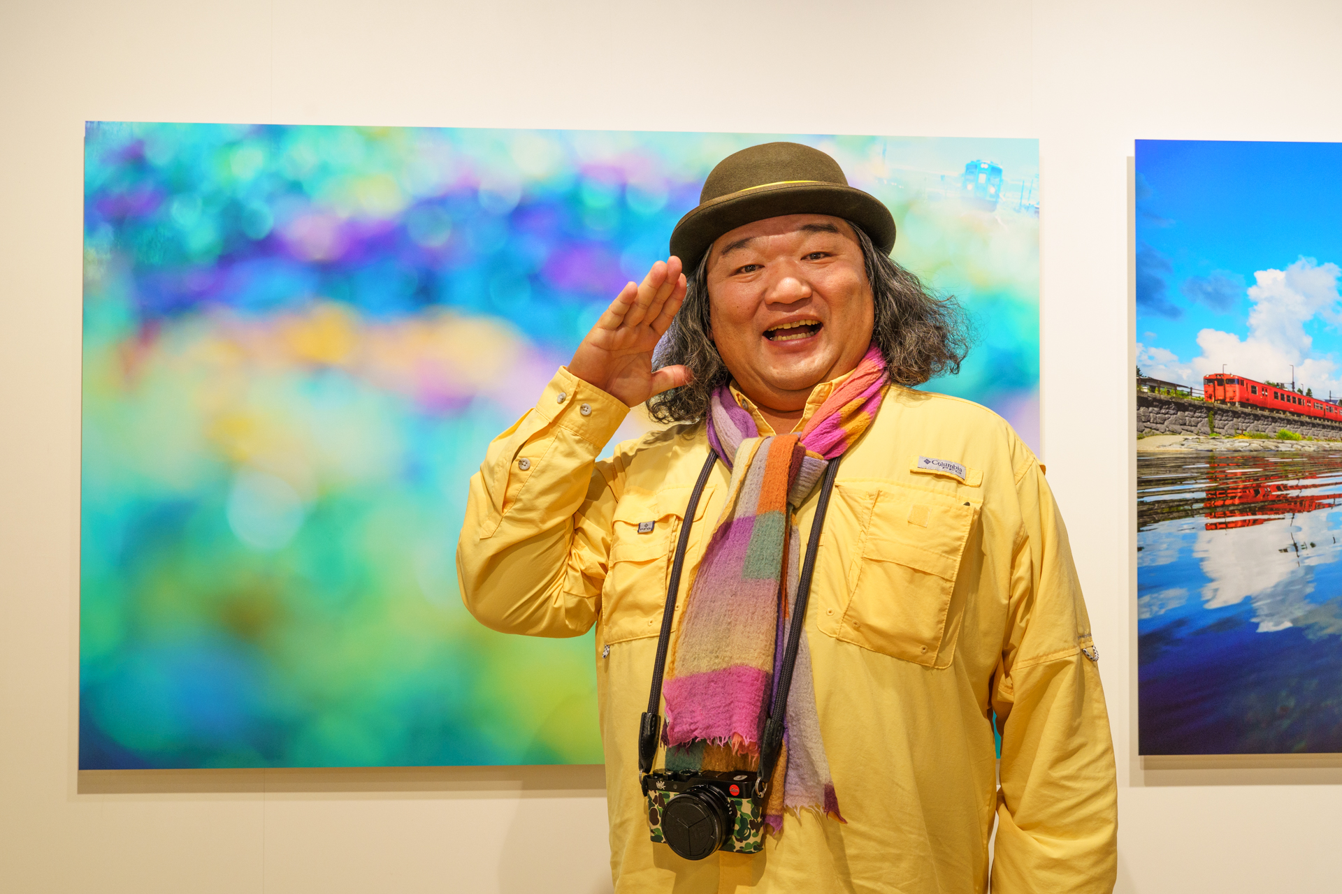 鉄道写真家の中井精也さん。写真展「今⽇もHappy Train！」の展示作品の前で