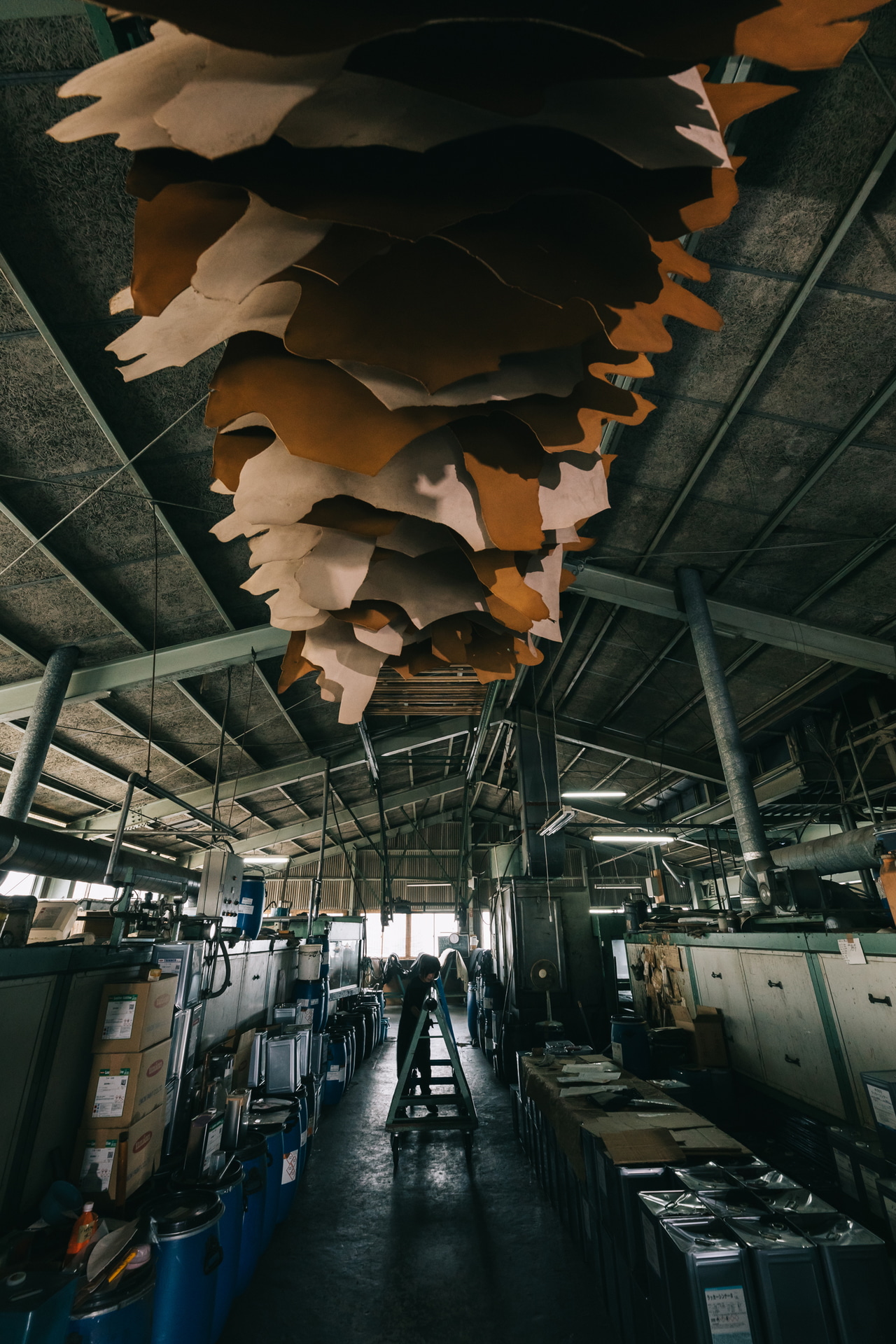 薄暗い工場内部で撮影。天井の乾燥レールに塗装が終わった革が干してある。三脚に固定すると手ブレの心配がなく、人の動きを見てシャッターが切れる<br><span class="fnt-85">キヤノン EOS 5D Mark IV／SIGMA 14-24mm F2.8 DG HSM｜Art／14mm／マニュアル露出（F8、1/30秒）／ISO 2000／WB：5,800K</span>