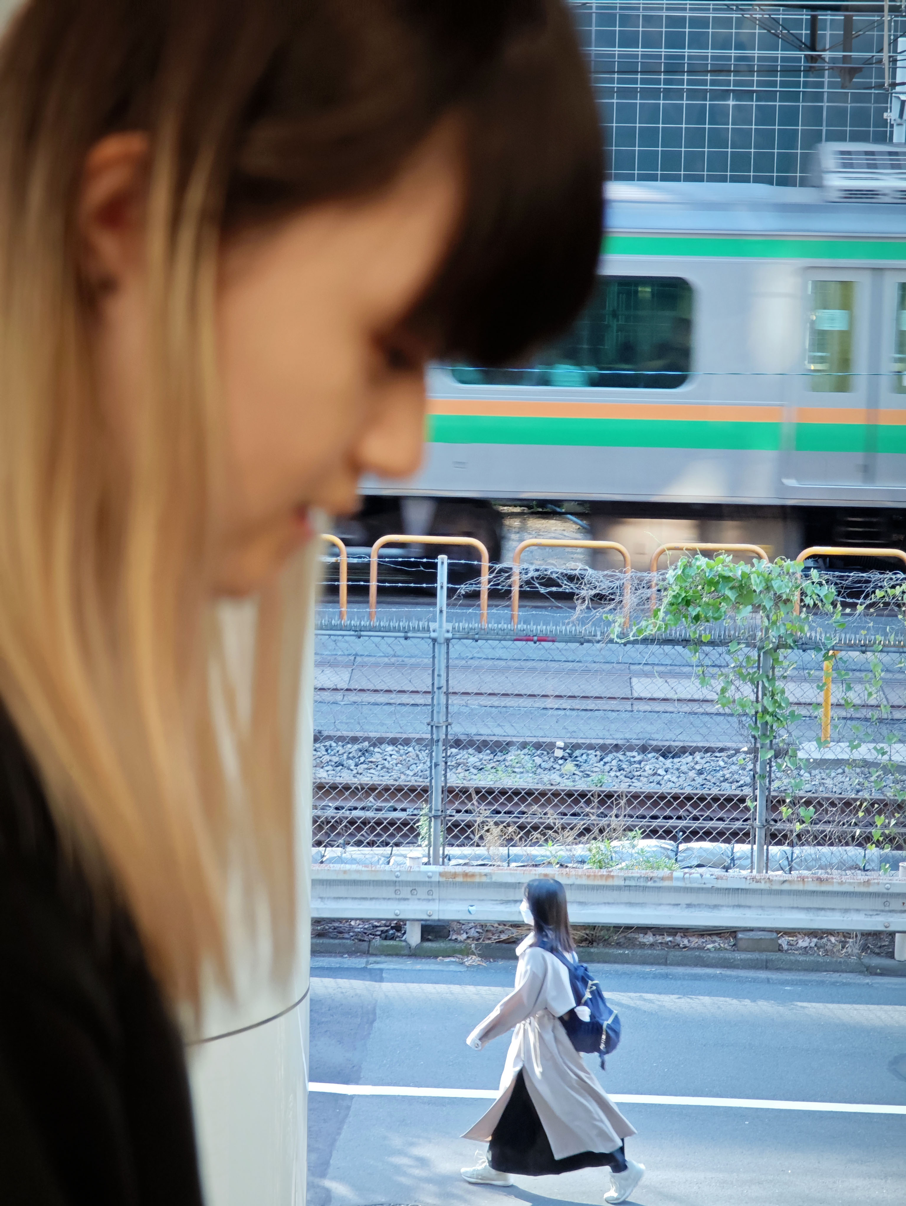 手前の人物を望遠レンズで大きくぼかし、奥に道を歩く人物を配置した。スマートフォンでは気になるシャッタータイムラグもほぼなく、狙ったタイミングで写し止められる<br><span class="fnt-85">120mm相当／絞り優先AE（F2.5、1/100秒、±0EV）／ISO 160／WB：オート</span>