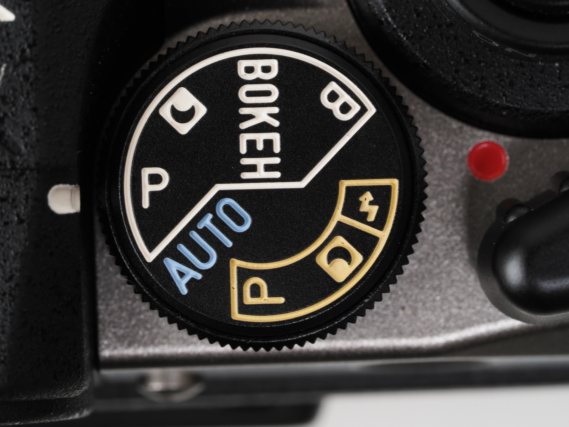 撮影モードダイヤルです。Pモード主体で、大きく分けて黄色がフラッシュモード、白色が通常モード。ボケや夜間撮影では表示のアイコン位置にセットします。AUTOはレンズ位置も固定されます。ちなみにこの文字の色、既視感があるなあと思っていたら、初期のSMC PENTAXの距離目盛りの色に似ています。またこのダイヤル、軽すぎますね。すぐに動いてしまうので注意しましょう。