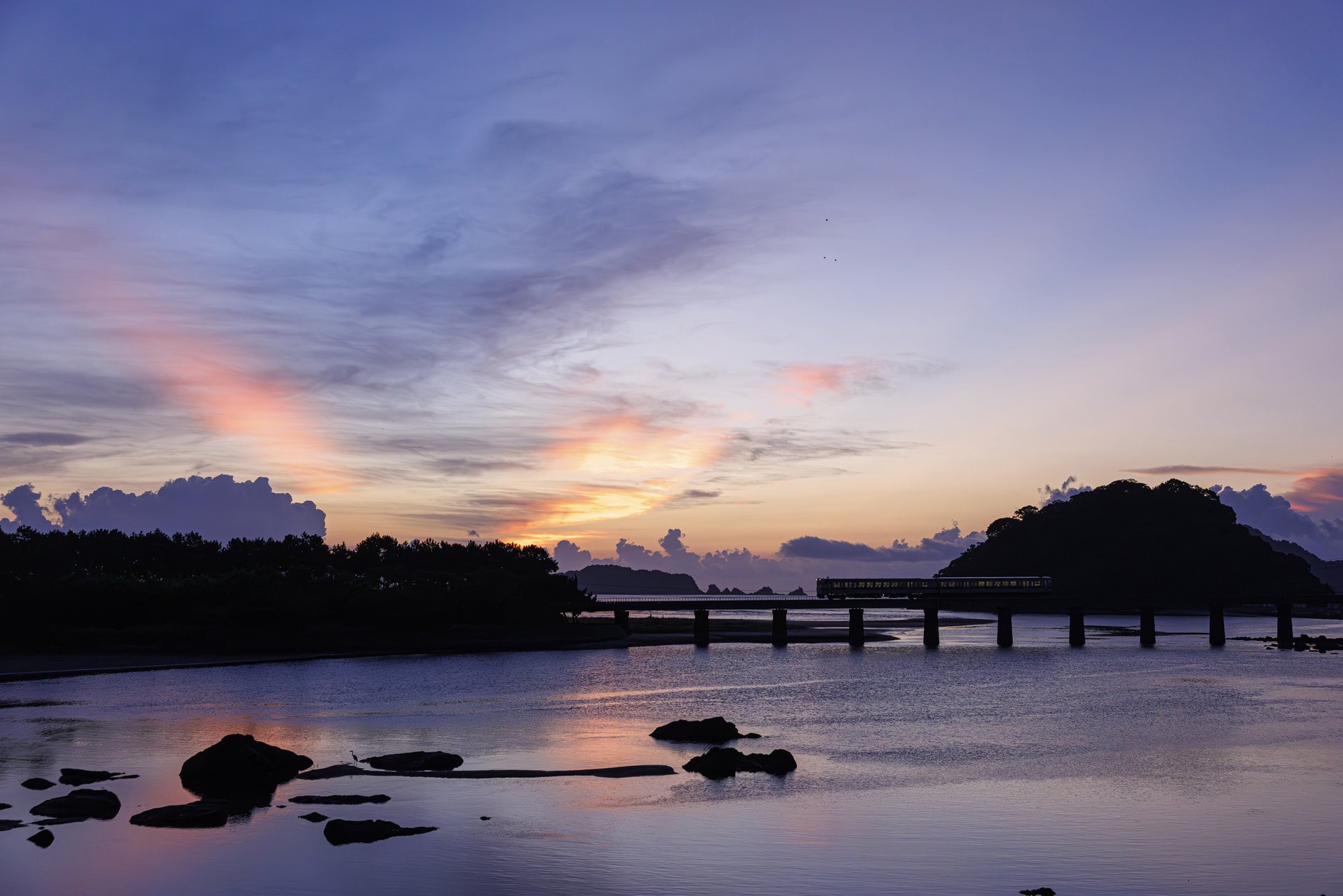 夜明けの日南線普通列車を狙っていると光の筋が出てきたので、アップの構図から光を入れた引きの構図に変更。撮影後、アップスケーリングしてアップの構図も切り出した<br><span class="fnt-85">キヤノン EOS R5 Mark II／RF28-70mm F2 L USM／40mm／マニュアル露出（F3.5、1/1,250秒）／ISO 3200／WB：オート</span>