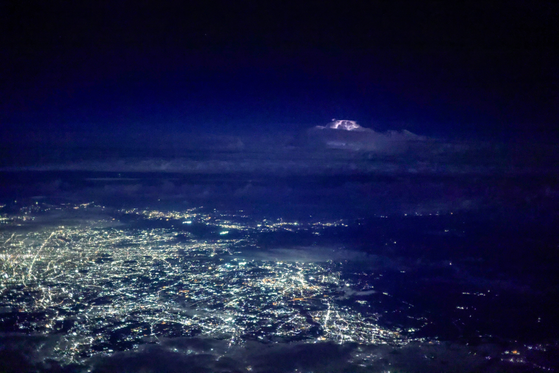 夜間飛行中に街灯りの奥の空が一瞬光った。雷だ！ 急いで「プリ連続撮影」モードにセットし、稲光を待つ。光った瞬間にシャッターボタンを押せばすべて記録されていた。30コマ/秒の撮影なので、大容量のカードがあった方が安心だ<br><span class="fnt-85">キヤノン EOS R5 Mark II／RF50mm F1.8 STM／50mm／絞り優先AE（F1.8、1/40秒、－0.3EV）／ISO 20000／WB：オート（B9）</span>