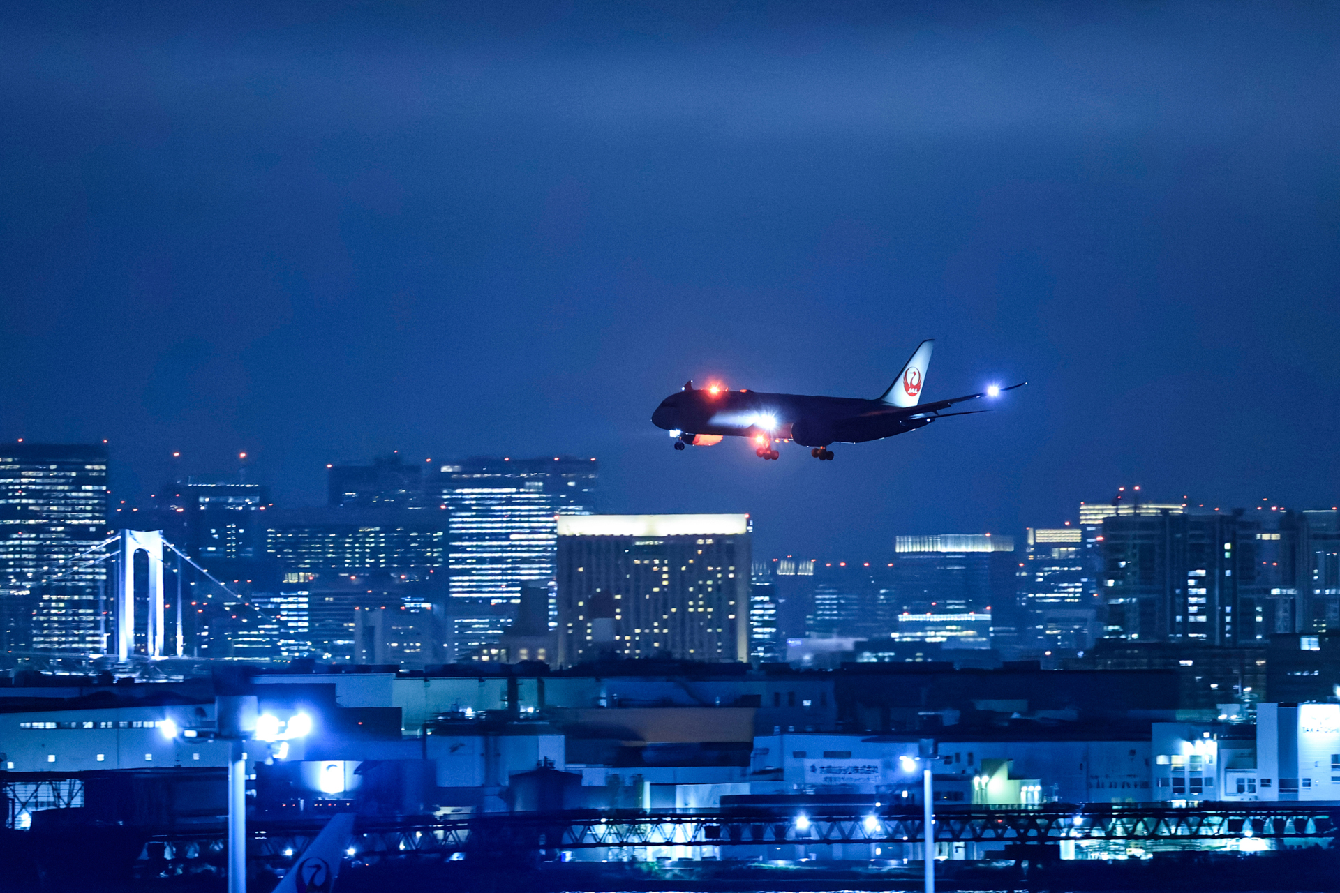 都心のビル群をバックにアプローチしてくる787を高速連写で追い、青白いライトと赤く点滅するライトが同時に光る瞬間を捉えた。カードへの書き込み速度が速いので、連写時に待つことがなく、撮影のストレスは感じない<br><span class="fnt-85">キヤノン EOS R5 Mark II／RF100-300mm F2.8 L IS USM／300mm（480mm相当）／絞り優先AE（F2.8、1/160秒、±0EV）／ISO 20000／WB：2,800K</span>