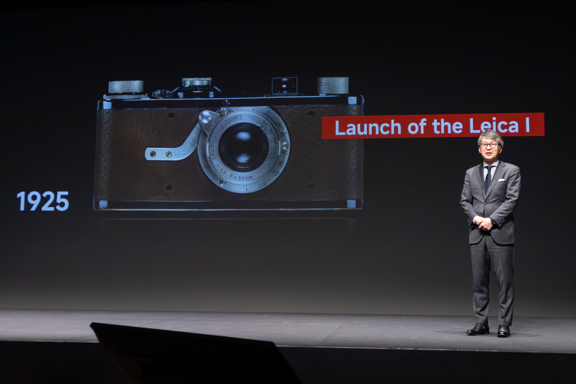 ライカカメラジャパンの福家一哲社長。スクリーンのカメラは、ライカ初の量産35mmカメラ「ライカI」