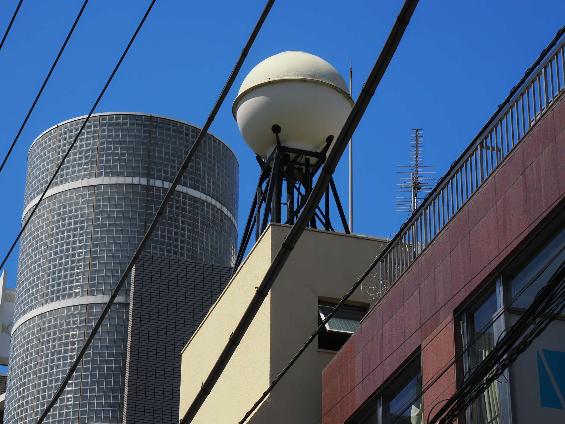 ビルの上の丸型の給水塔も好物でして、見つけると撮影しちゃうわけです。青空に玉が映えます。<br><span class="fnt-85">OM SYSTEM OM-3／M.ZUIKO DIGITAL ED 12-100mm F4.0 IS PRO／54mm（108mm相当）／プログラムAE（1/640秒、F11、−0.7EV）／ISO 400</span>
