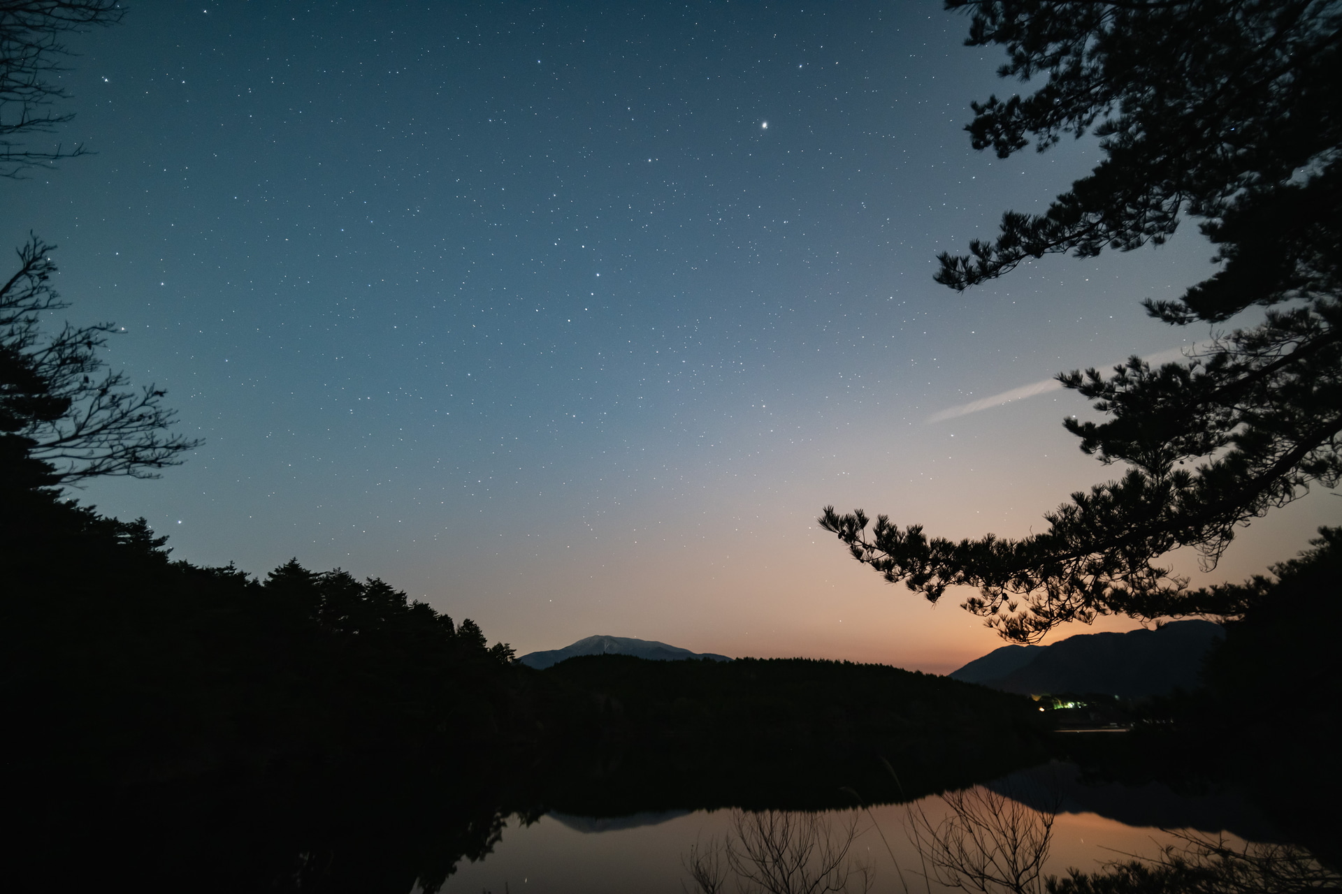 きょうは美しく静かな湖の夜空。春の星空は冬の星空に比べて地味なんだけど、見どころは多いのです。真ん中あたりにCを反転したような星の並びがわかるかな。かんむり座という星座なんだけどここには反復新星と言われる星がありまして、普段は10等級（肉眼では見えない）なんだけど急激に2等級まで明るくなるんです。その現象が近々起きると予測されてて、いま注目している星座なんですよ。<a href="https://www.ananscience.jp/variablestar/?page_id=624">詳しくはこちらをどうぞ</a>。<br><br>ほかにも春の夜空にはかみのけ座銀河団やらおとめ座銀河団などと呼ばれるものや、メシエ13という球状星団なるものがありまして、星景写真というよりは天体望遠鏡を使っての見どころ盛りだくさんなんです。宇宙の神秘を直接感じられる良さがあるんですね。Wikipediaを見てるだけでも楽しめますけど、ぜひご近所で公開天文台を探してみてください。やはり肉眼で見て感じることが1番です。<br><br>ここは岐阜県、保古の湖。空が赤いのは山の向こうに月が上がってきたから。こういうタイミングの空の美しさは格別です。そうしたこともその現場で感じてこそですよね。ぜひ訪れてみてください