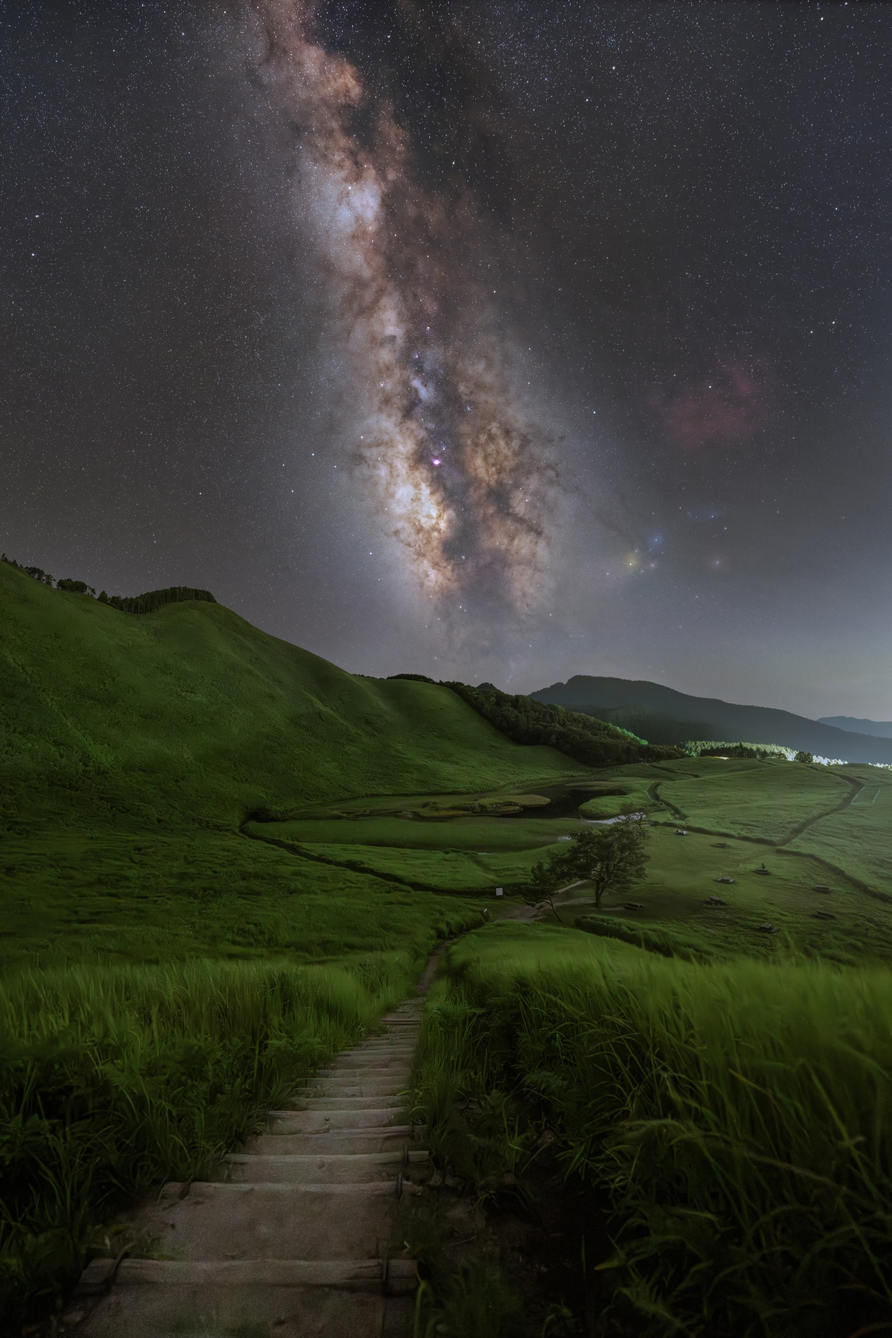 曽爾高原で撮影。一面に広がる緑の草原と、夏の夜空に凛と立ち昇る天の川が織りなす光景を、階段を少し登った高所から俯瞰の構図で捉えた。足場が限られる場所でも、三脚の安定性のおかげで構図決めから撮影までスムーズだ<br><span class="fnt-85">ソニー α7R V／FE 14mm F1.8 GM／14mm／マニュアル露出／WB：オート<br>星空（F3.5、120秒、ISO 2000）<br>地上（F2、10秒、ISO 8000）</span>