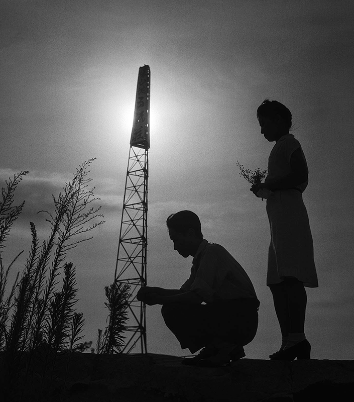 撮影者：吉田潤<br>撮影年：不明<br>撮影地：広島県<br>タイトル：広島中島 黙祷の花束を捧げる<br>所有者：日本写真保存センター<br>所蔵：日本写真保存センター
