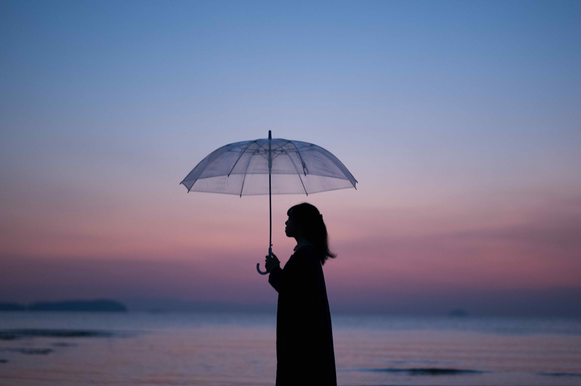 波の音が静かに響く海辺。シルエットとして描いた人物は影絵のよう。淡い夕暮れの空を背景にして透明の傘に映る空のソフトなグラデーションは、ズミルックスレンズならでは<br><span class="fnt-85">ライカM EV1／ライカ ズミルックスM f1.4/50mm ASPH. ／50mm ／マニュアル露出（F1.7、 1/90秒）／ ISO 1000／ WB：白熱灯</span>